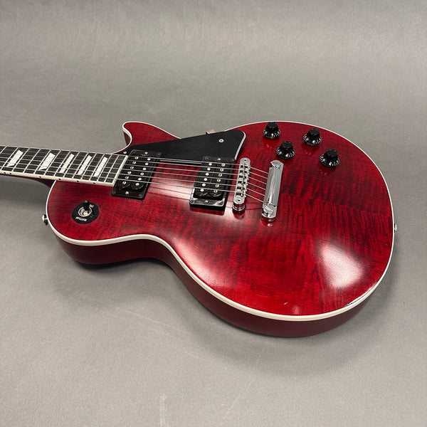 Close-up of red electric guitar with dual humbucker pickups, black pickguard, and four black control knobs on gray background