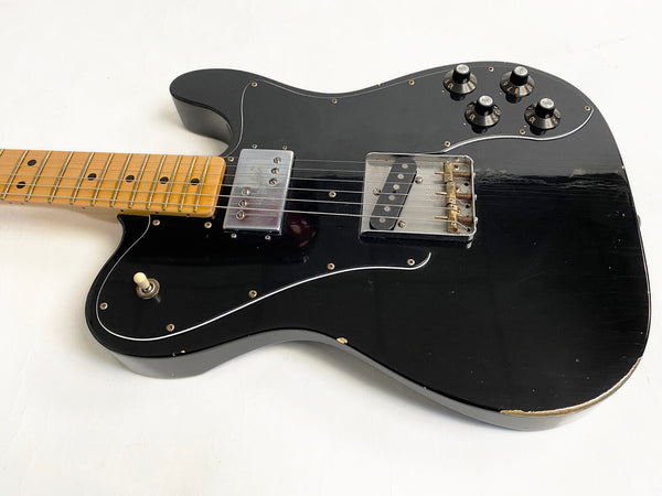 Black electric guitar with maple neck and fretboard, two pickups, four control knobs, and a white toggle switch on a white background