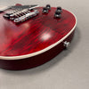 Close-up of red electric guitar body with flamed maple top, chrome bridge, and black control knobs on gray background