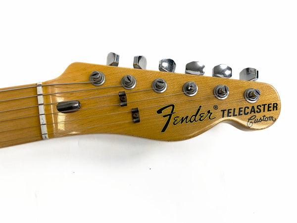 Close-up of natural wood Fender Telecaster Custom guitar headstock with six tuning pegs and strings on white background