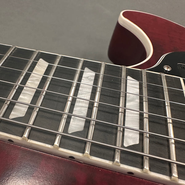 Close-up of electric guitar fretboard with pearloid block inlays and metal frets on a cherry red guitar body