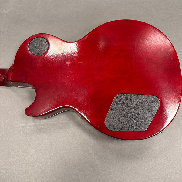 Back view of red electric guitar body with control cavity covers and smooth glossy finish on gray background