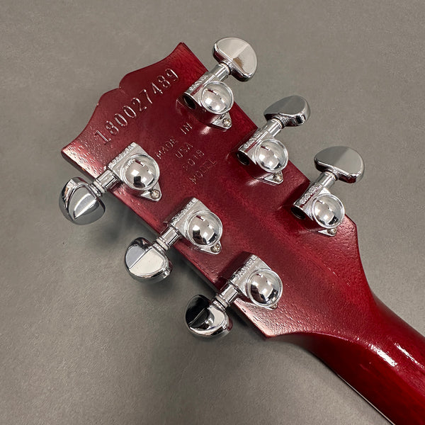 Back of cherry red guitar headstock with six silver tuning pegs, serial number 180027489, made in USA 2018 model stamped on wood