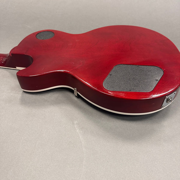 Back side view of cherry red electric guitar body with black control cavity covers and white binding on grey background