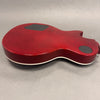 Back view of red electric guitar body with white binding and black control cavity covers on gray background