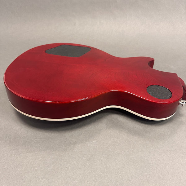 Back view of red electric guitar body with white binding and black control cavity covers on gray background