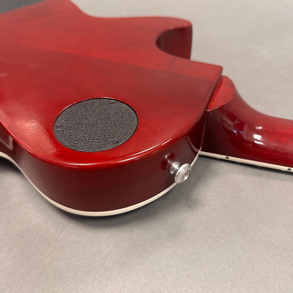 Close-up of the back of a red electric guitar showing the control cavity cover and strap button on a gray background