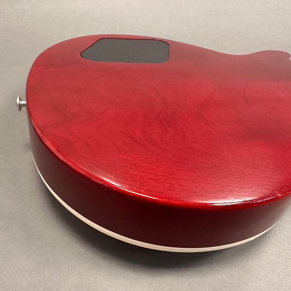 Close-up of red electric guitar body back showing wood grain and cream binding with control cavity cover and strap button