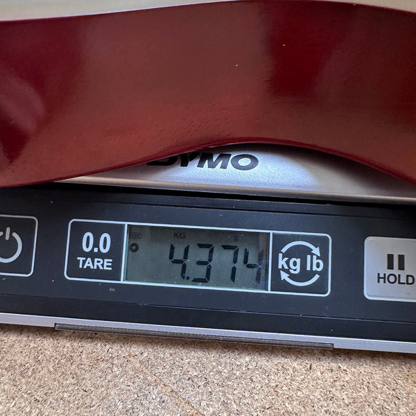 Close-up of a digital scale showing the weight of a guitar at 4.374 kilograms with the edge of a red guitar body visible on top of the scale.