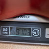 Digital scale displaying guitar weight as 9 pounds 10.3 ounces with partial view of guitar body and DYMO branding.