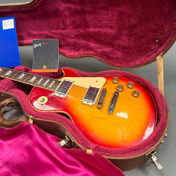 Gibson Les Paul electric guitar with sunburst finish in pink-lined hardshell case with Gibson tag and blue warranty card.