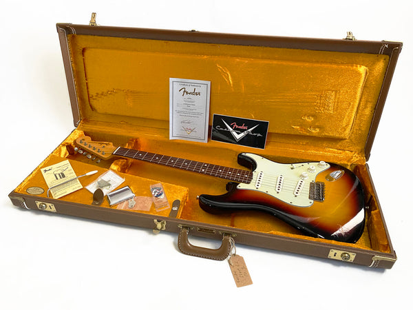 Vintage Fender Stratocaster electric guitar in sunburst finish with original brown hard case and accessories including certificate of authenticity and Fender instructional materials