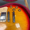 Close-up of sunburst electric guitar body showing chrome bridge, tailpiece, cream-colored pickup cover, and four gold tone control knobs with numbers, resting in a plush red lined guitar case interior