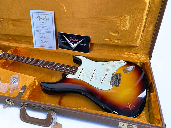 Fender Custom Shop Stratocaster electric guitar in sunburst finish inside vintage brown hardshell case with orange interior, includes Fender Custom Shop Certificate of Authenticity and accessories.