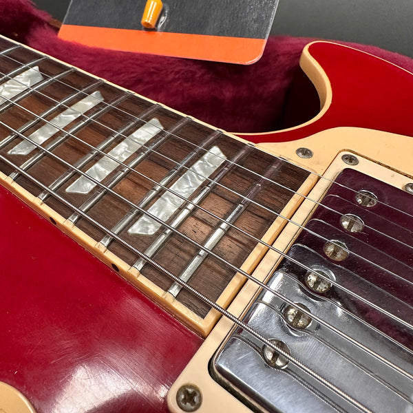Close-up of red electric guitar fretboard with mother-of-pearl inlays and chrome pickup covers on vintage style guitar