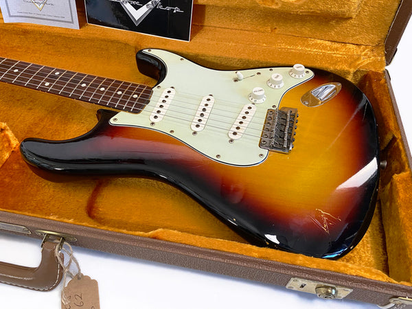 Vintage Fender Stratocaster electric guitar in sunburst finish inside orange plush-lined hardshell case with volume and tone knobs visible