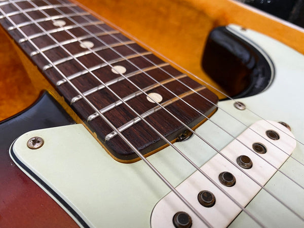 Close-up of electric guitar frets, steel strings, and white single-coil pickups with sunburst finish body and white pickguard.