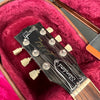 Close-up of Gibson Les Paul Standard guitar headstock with vintage tuning pegs resting in red velvet guitar case interior.