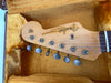 Close-up of Fender Stratocaster guitar headstock with vintage tuning pegs in a plush yellow guitar case interior