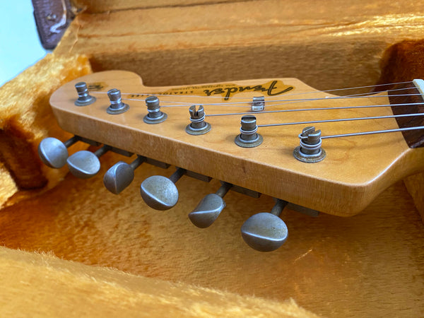 Close-up of Fender Stratocaster guitar headstock with six tuning pegs and strings inside plush yellow guitar case