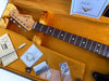 Fender Stratocaster guitar neck and headstock with rosewood fretboard inside vintage orange velvet-lined hard case, showing included tremolo springs diagram, tuning keys, metal tremolo cover, and custom Fender certificate