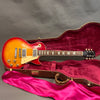Vintage sunburst Gibson Les Paul Standard electric guitar in open brown hardshell case with red plush interior and pink satin lining, showcasing classic body design and dual humbucker pickups.