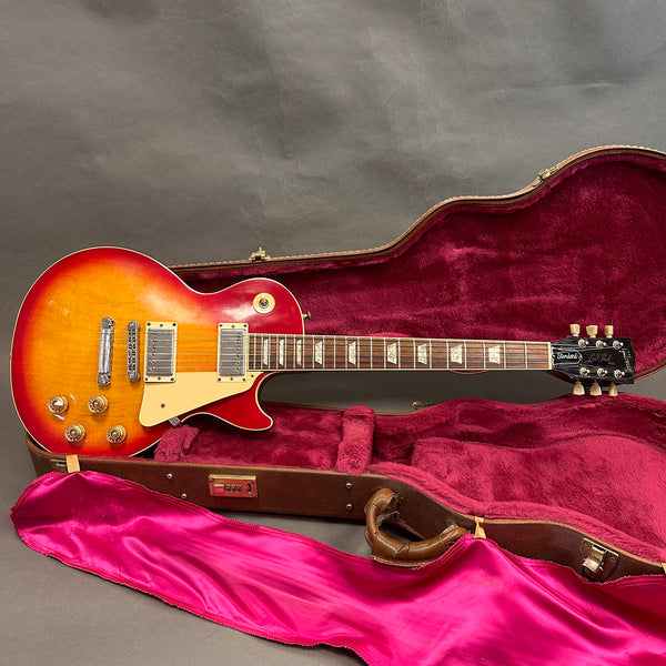 Vintage sunburst Gibson Les Paul Standard electric guitar in open brown hardshell case with red plush interior and pink satin lining, showcasing classic body design and dual humbucker pickups.
