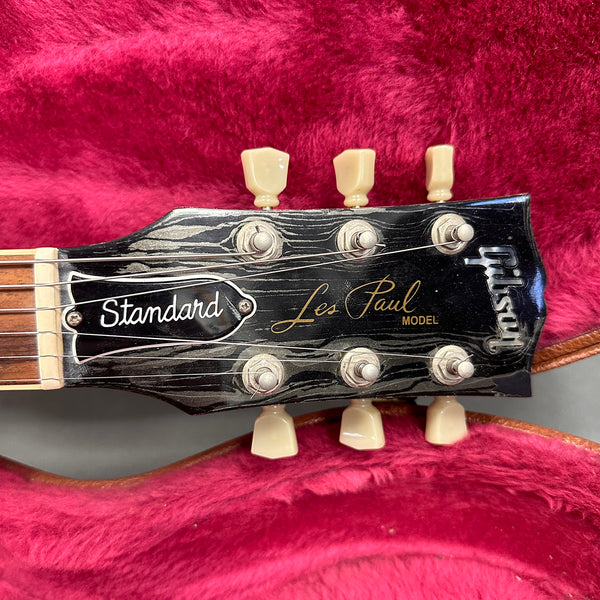 Close-up of Gibson Les Paul Standard guitar headstock with tuning pegs on red plush guitar case lining