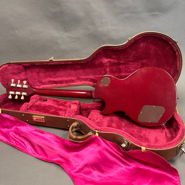 Rear view of cherry red electric guitar inside vintage hard shell guitar case with plush red interior and pink satin cover