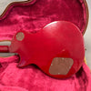 Back view of red electric guitar body with brown plastic control cavity covers inside a red plush-lined guitar case