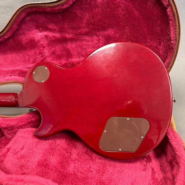 Back view of red electric guitar body with brown plastic control cavity covers inside a red plush-lined guitar case