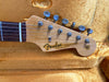 Close-up of vintage Fender Stratocaster guitar headstock with six tuning pegs, rosewood fretboard, and original contour body decal, resting on a plush orange guitar case interior.