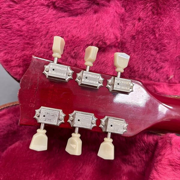 Close-up of vintage red guitar headstock with six vintage tuning pegs on plush pink guitar case lining