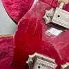 Close-up of red guitar headstock showing metal tuning pegs, a visible crack, and embossed "MADE IN USA" marking, against a pink plush background inside a guitar case.
