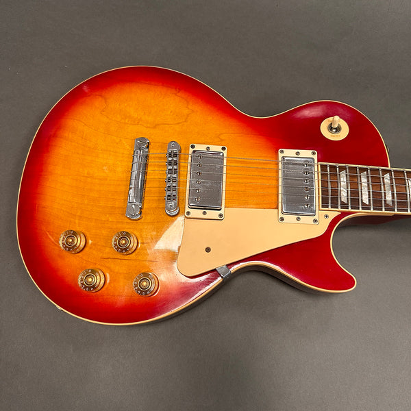 Close-up of a sunburst electric guitar body with dual humbucker pickups, four control knobs, and a cream pickguard on a grey background