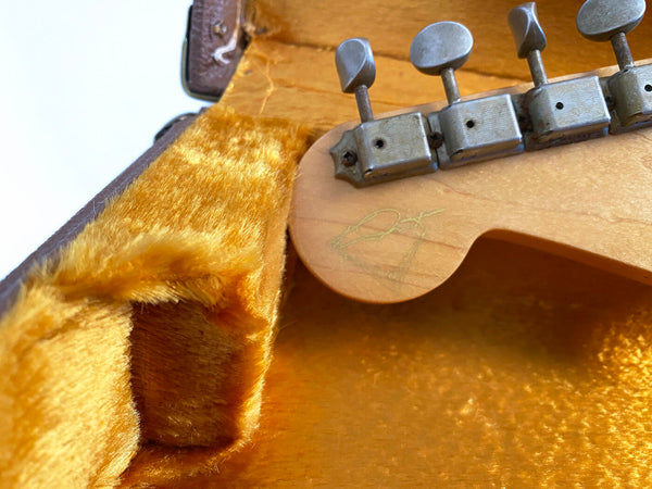 Close-up of vintage guitar tuning pegs and signed wooden headstock inside plush yellow guitar case lining