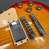 Close-up of electric guitar chrome humbucker pickup, bridge, tailpiece, and gold tone control knobs on sunburst finish body