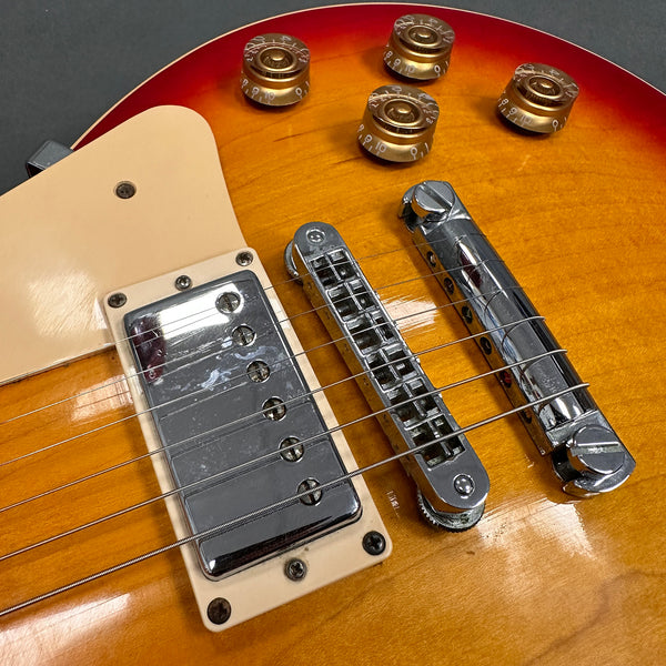 Close-up of electric guitar chrome humbucker pickup, bridge, tailpiece, and gold tone control knobs on sunburst finish body