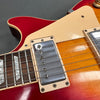 Close-up image of electric guitar body showing humbucker pickup, cream pickguard, rosewood fretboard with mother-of-pearl inlays, and sunburst finish on red and orange guitar top.