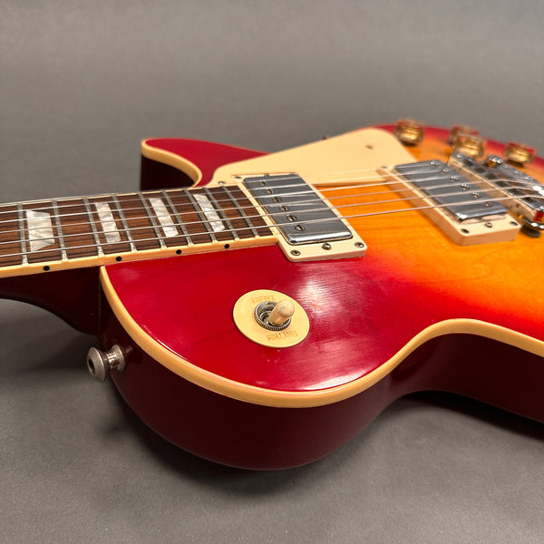 Close-up of red sunburst electric guitar body with cream pickguard, chrome humbucker pickups, and maple neck with inlaid fret markers on gray background