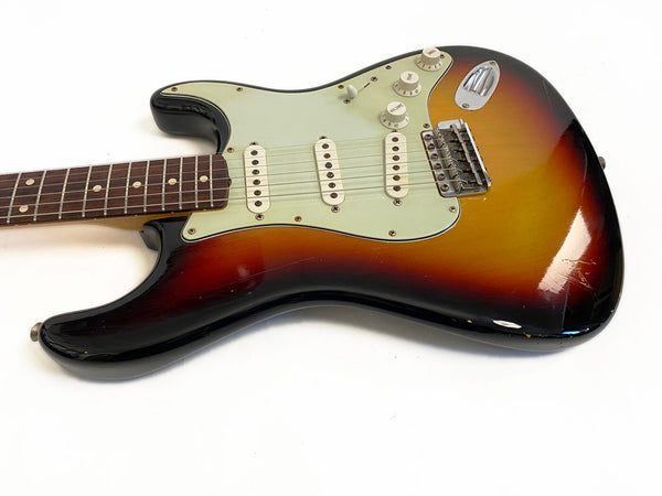 Close-up of a vintage sunburst electric guitar body with three single-coil pickups, white pickguard, volume and tone knobs, and rosewood fretboard against a white background.