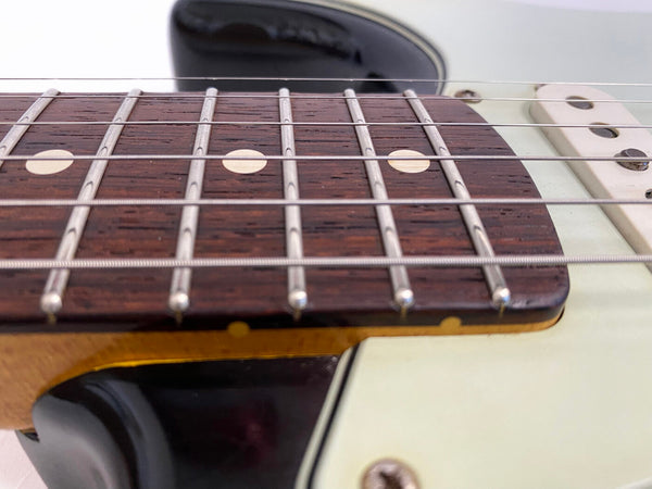 Close-up of electric guitar neck and fretboard with metal frets, dot inlays, and guitar strings on cream-colored body and black pickguard