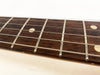 Close-up of guitar fretboard showing metal frets, dot position markers, and steel guitar strings on dark wood fingerboard