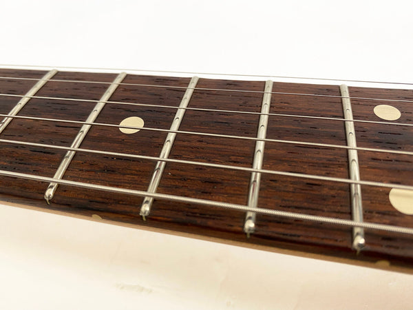 Close-up of guitar fretboard showing metal frets, dot position markers, and steel guitar strings on dark wood fingerboard