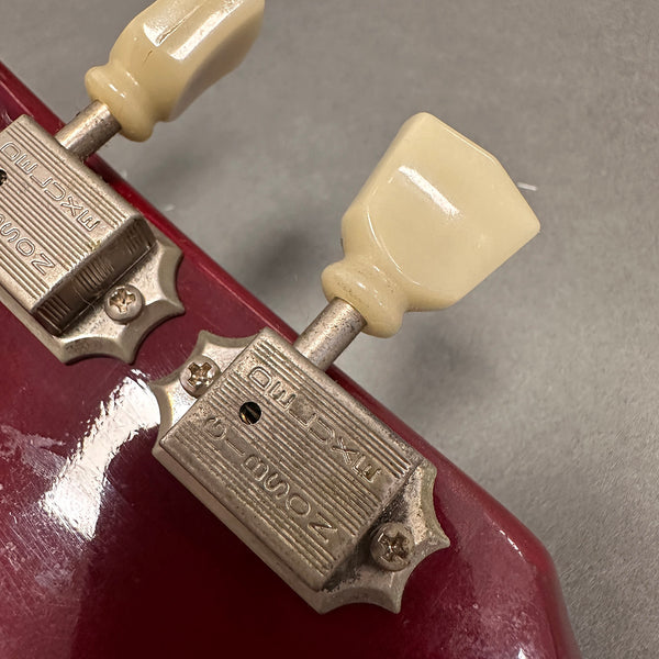Close-up of vintage Zount Zonmark guitar tuners with cream plastic tuning pegs on red guitar headstock