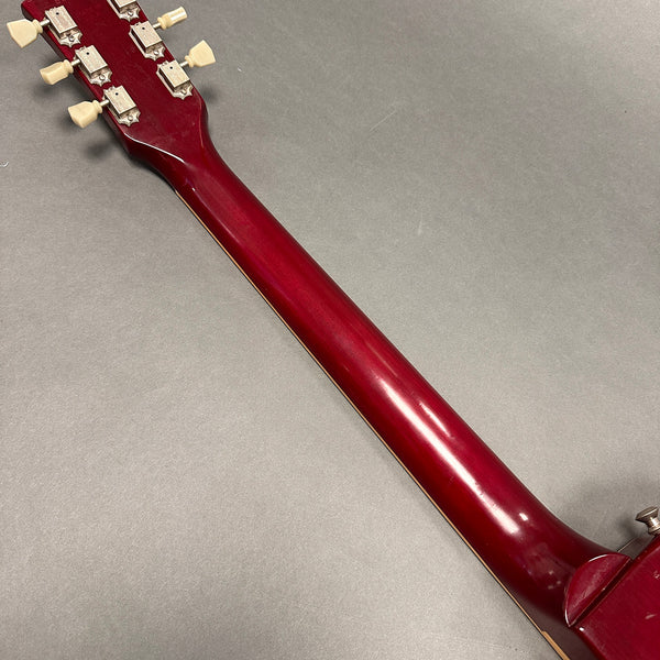 Close-up of a red finished guitar neck and tuning pegs on a gray background
