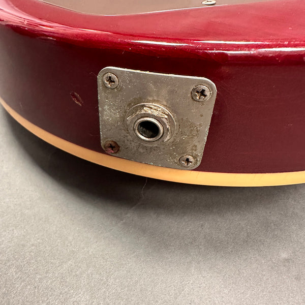 Close-up of vintage red electric guitar input jack plate with cream binding and visible wear on metal parts