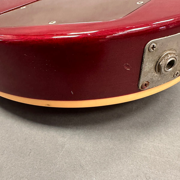 Close-up of vintage red electric guitar body showing metal input jack plate and cream binding with minor finish wear and scratches