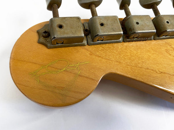 Close-up of vintage guitar headstock showing aged metal tuning machines and faded autograph on maple wood finish