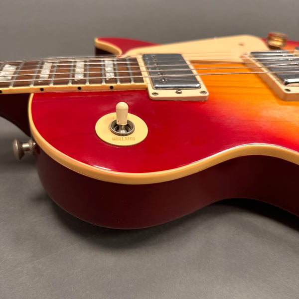 Close-up of red and sunburst electric guitar body with cream binding, pickup switch, and humbucker pickups on gray background